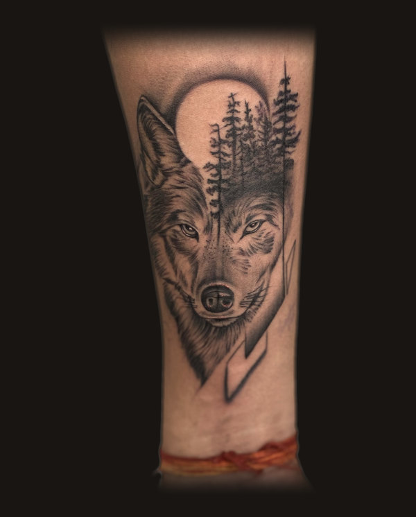 Wolf with forest, black and grey tattoo on a forearm